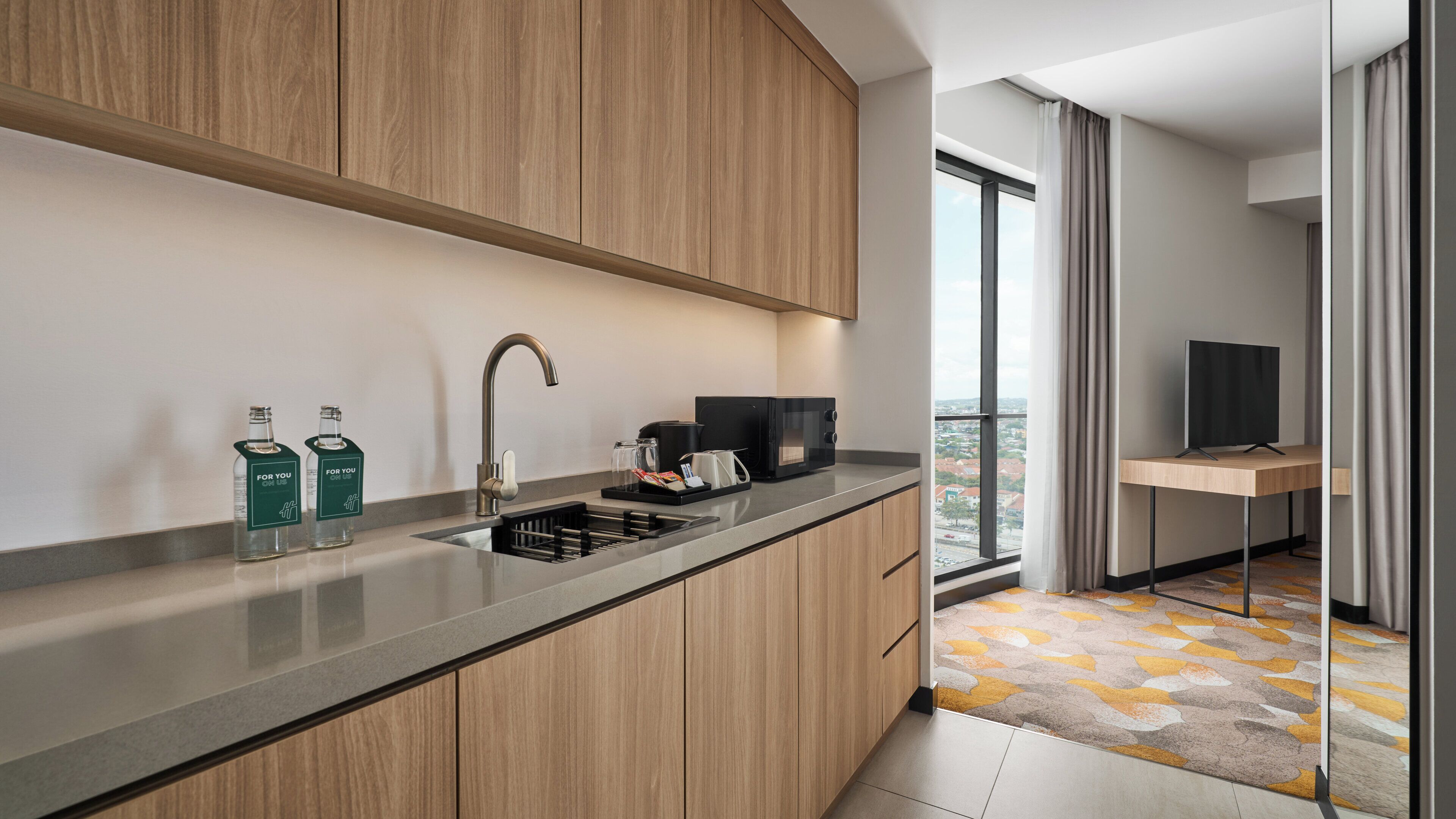 A modern kitchen with a built-in sink, wooden cabinets, and a view of the city through a large window.