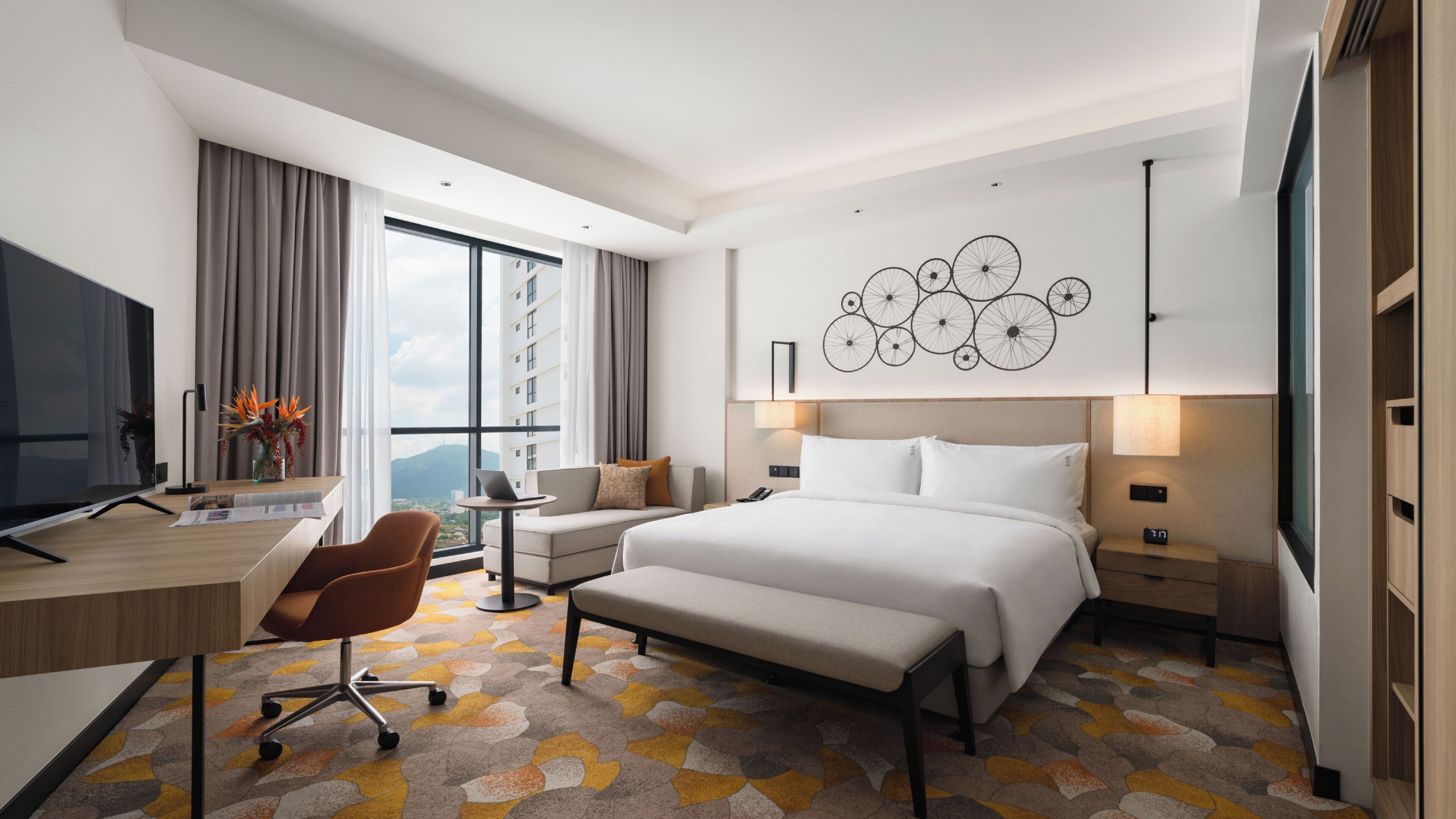 Habitación de hotel moderna con una cama grande, un escritorio con una computadora portátil, un televisor y vista a la ciudad.