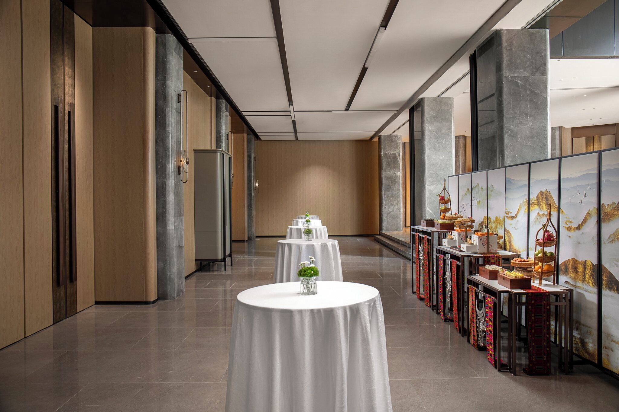 A corridor with round tables, a wall with a mural, and a buffet setup.