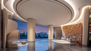 A modern lobby with a curved ceiling, a reception desk, and a seating area with a view of the city skyline. - Crowne Plaza Sanya Yazhou Bay by IHG (Sanya)