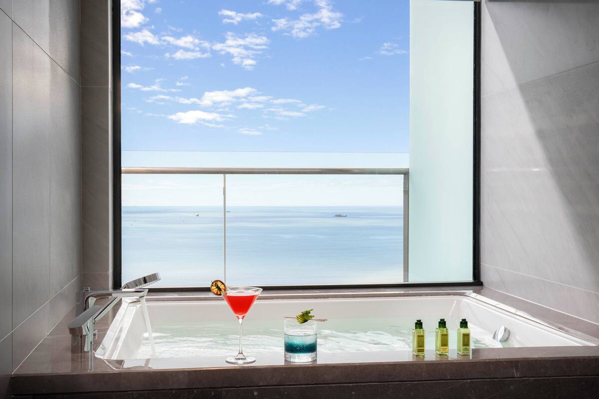 Un baño moderno con una bañera grande, un cóctel rojo y un vaso de bebida azul.
