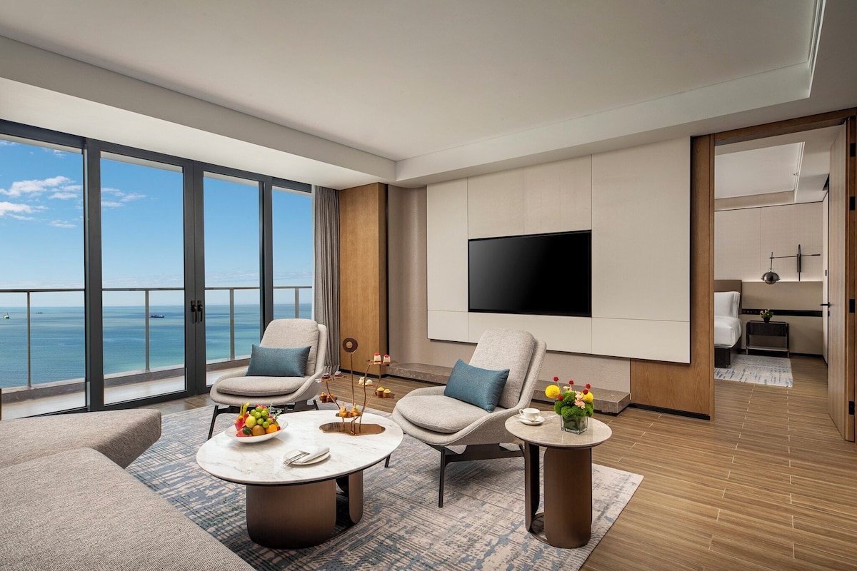 Una habitación de hotel moderna con un balcón grande, un televisor de pantalla plana y una zona de comedor con una mesa dispuesta para dos.
