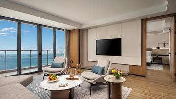 A modern hotel room with a large balcony, a flat-screen TV, and a dining area with a table set for two.