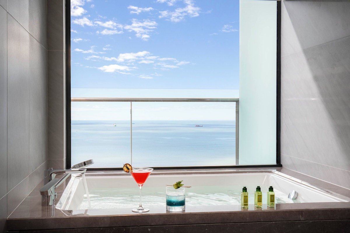 Un baño moderno con una bañera grande, un cóctel rojo y un vaso de bebida azul.