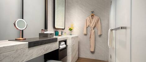 A modern bathroom with a marble vanity, a round mirror, a robe hanging on the wall, and a shower area.