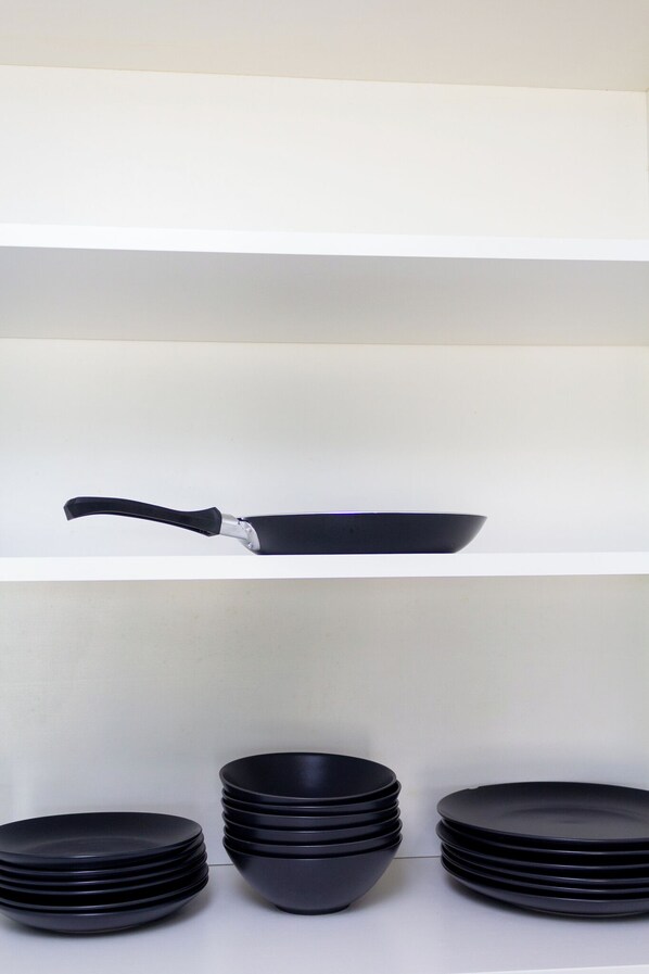 A kitchen with a black frying pan on a white shelf and several black bowls stacked on the counter.