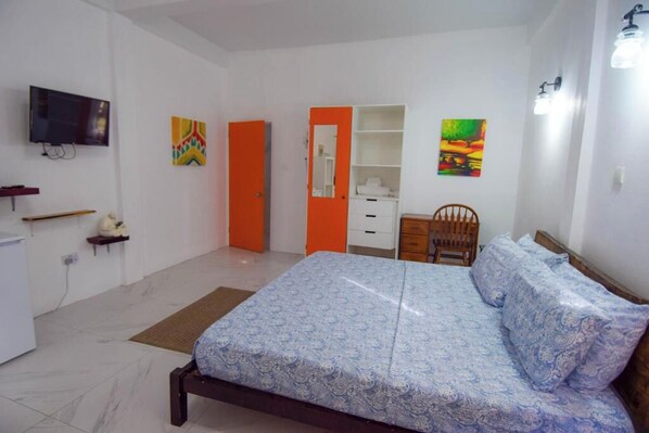 A bedroom with a bed, a TV, a wardrobe, a chair, and artwork on the walls.