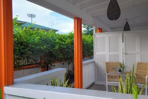 A covered outdoor seating area with a white door, orange columns, and a view of greenery and a building in the background.