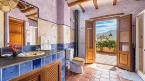 A bathroom with a large mirror, a sink, and a toilet. There is a window with a view of a building and a garden.