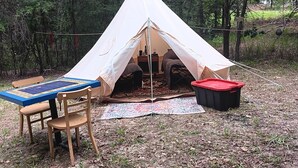 A tent set up in a forest with a table and chairs nearby.