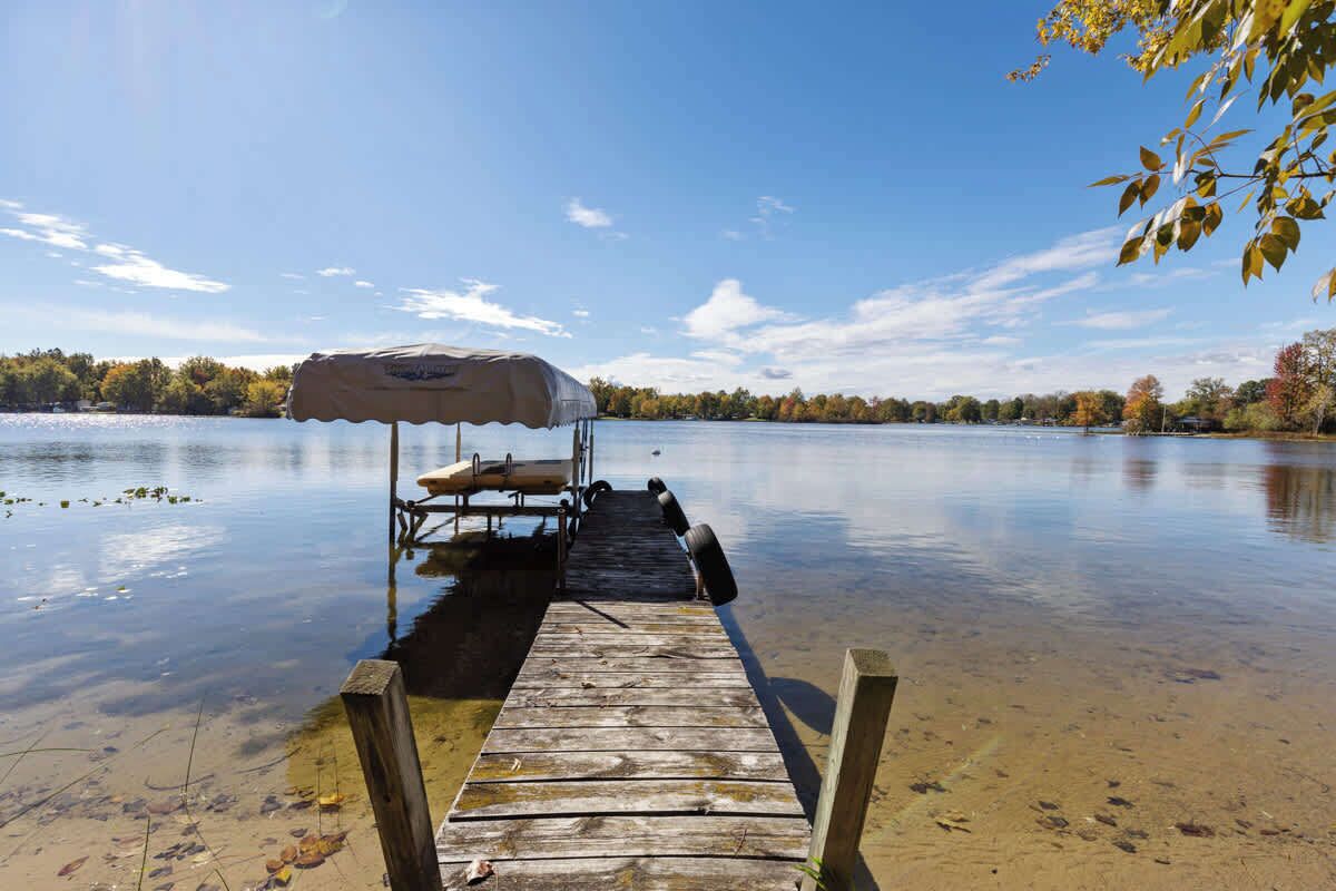 A wooden dock extending into a calm lake with a covered boat and a canopy.