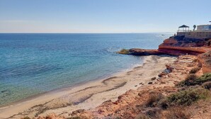 Une plage côtière aux eaux bleues et limpides, avec un rivage sablonneux et une construction dotée d’un toit, située au sommet de la falaise.