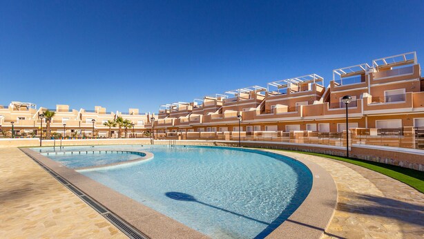 Un hôtel moderne doté d’une piscine, de nombreux balcons et offrant une vue sur un ciel d’un bleu éclatant.