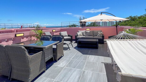 Tagterrasse med fletmøbler, et bord og en stor parasol.