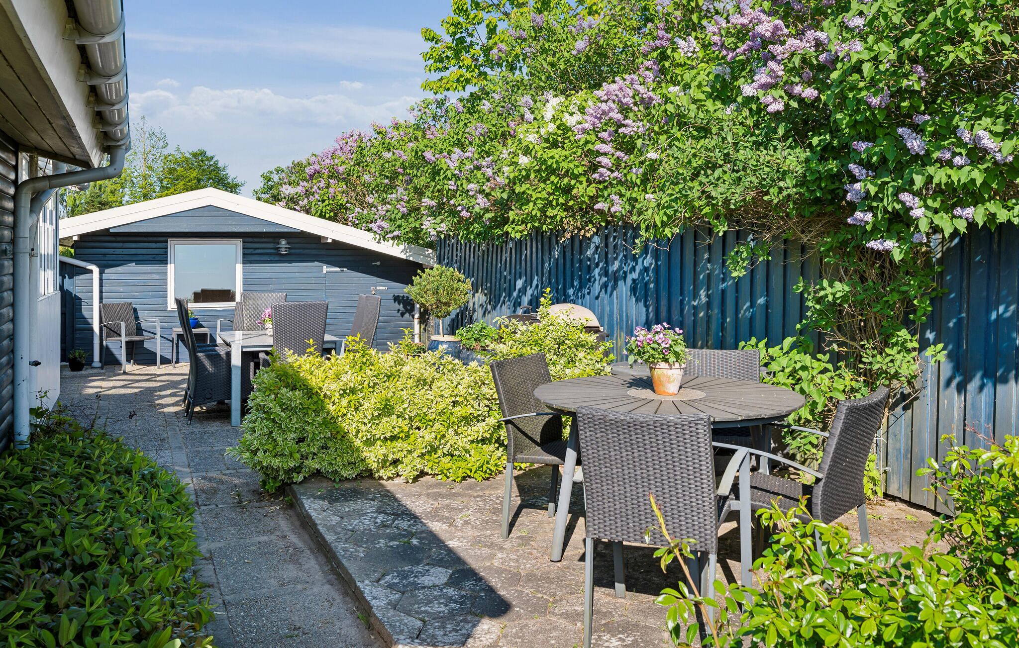 Een terras met een tafel en stoelen, een kleine schuur en een blauwe omheining.