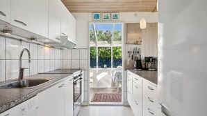 Een moderne keuken met witte kastjes, een roestvrijstalen spoelbak en een inbouwoven. Er is een raam met uitzicht op een tuin en een deur naar een buitenruimte.