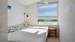 Een slaapkamer met een bed, een stoel, een raam met uitzicht op zee en een wandlamp.