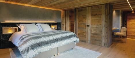 A modern bedroom with a large bed, wooden ceiling beams, and a built-in wardrobe.