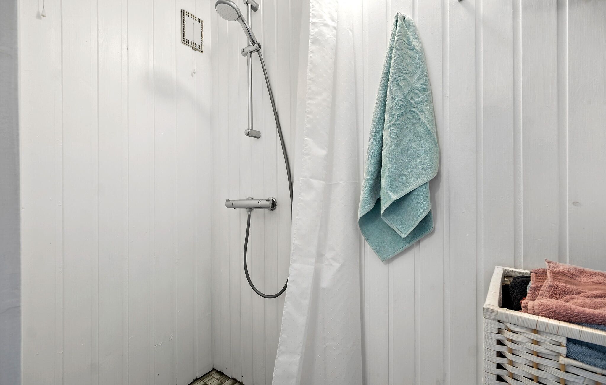 En dusch med ett handhållet duschmunstycke, en väggmonterad kontrollpanel och ett vitt duschdraperi.