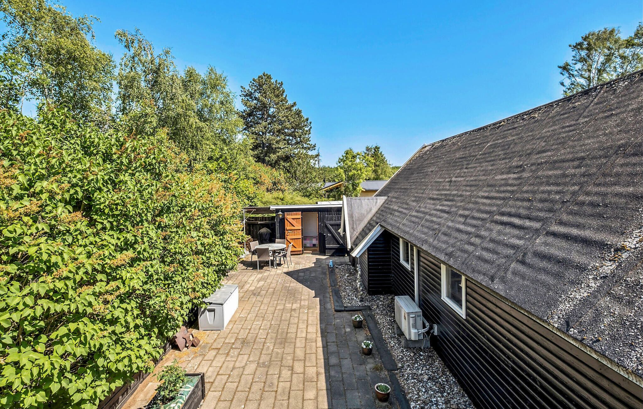 Une maison moderne avec un toit en pente, une terrasse dallée et un jardin luxuriant.
