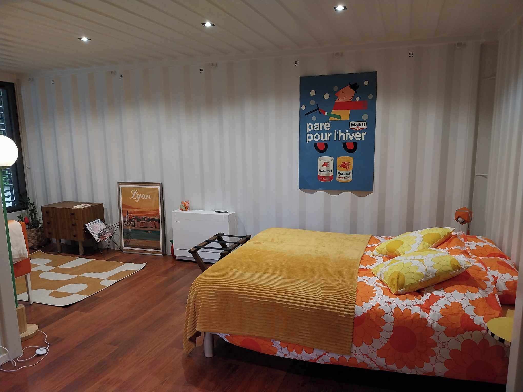 A bedroom with a bed, a small table, a chair, a radiator, and a poster on the wall.