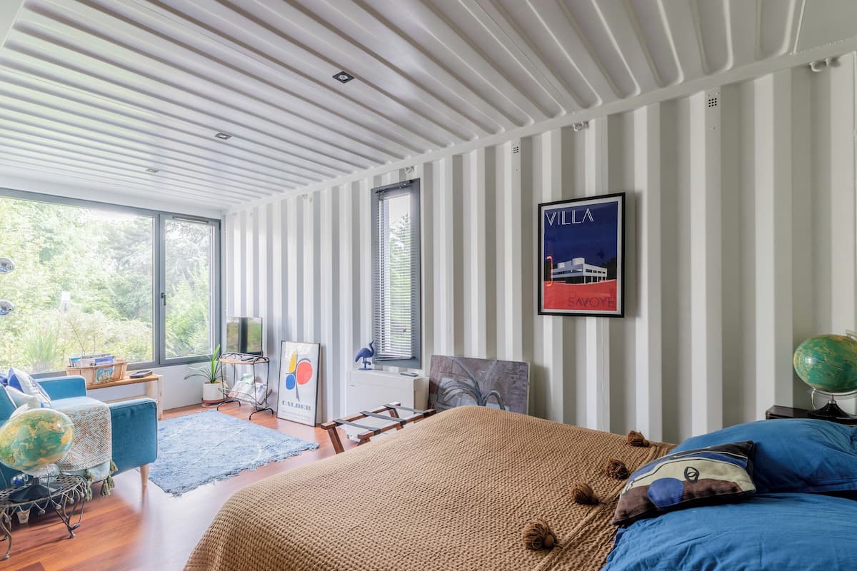 Un dormitorio moderno con una cama grande, un sofá azul, un globo terráqueo y una ventana con vistas a zonas verdes.
