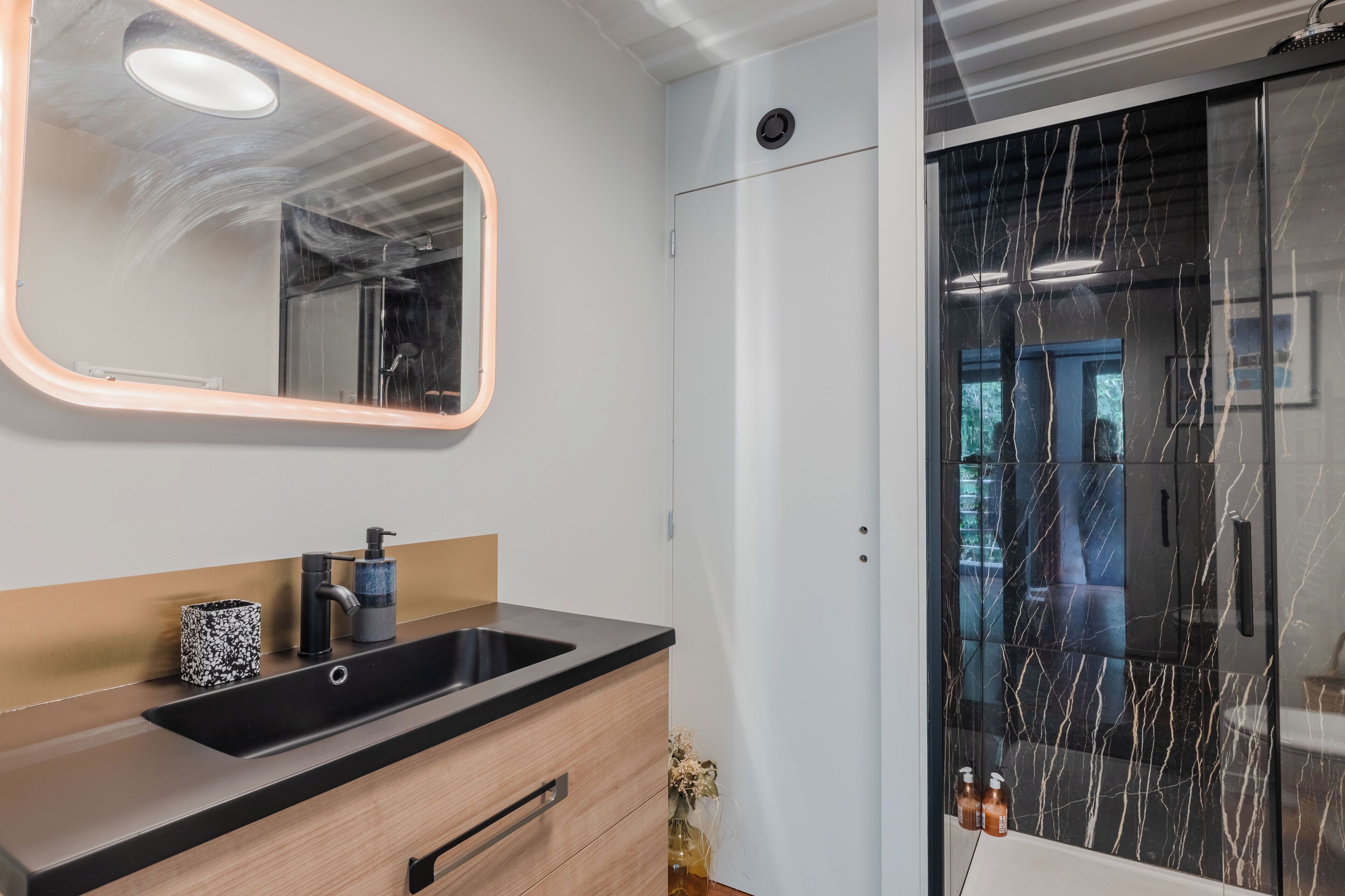 A modern bathroom with a large mirror, a sink, and a shower area.