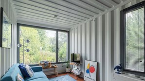 Una sala moderna con un sofá azul, una mesa de centro, un televisor y un amplio ventanal con persianas.