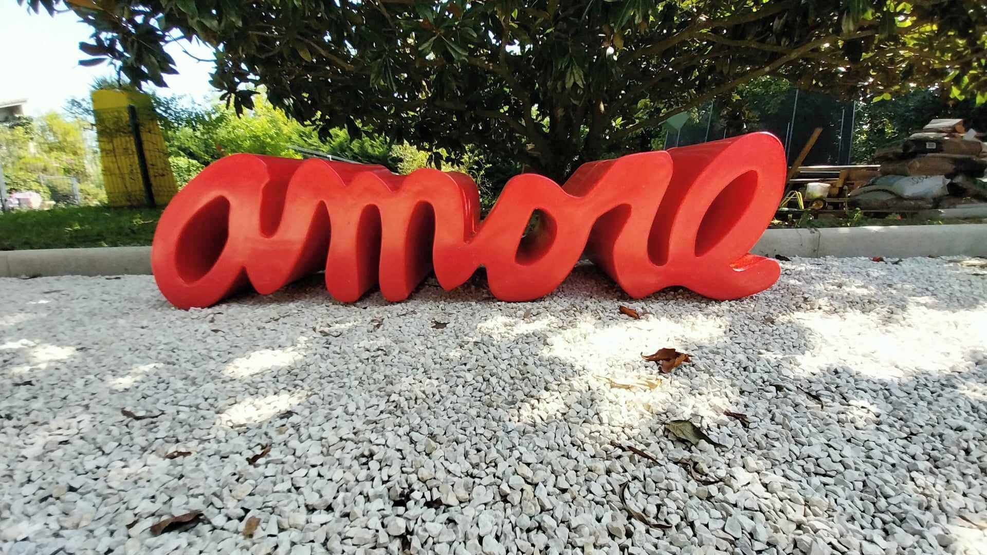 Das dreidimensionale Wort 'Amore' in roter Farbe auf einem Kiesuntergrund.