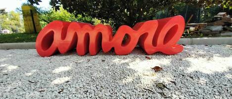 Das dreidimensionale Wort 'Amore' in roter Farbe auf einem Kiesuntergrund.