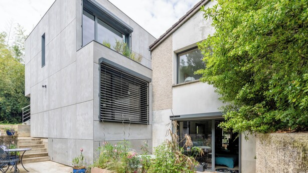 Una casa moderna de dos pisos con techo plano, ventanas grandes y balcón.