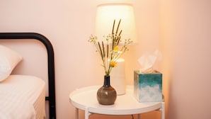 Ein Nachttisch mit Blumen in einer Vase, einer Taschentuchbox und einer Lampe in einem Hotelzimmer.