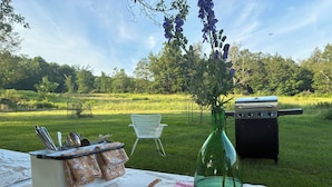 Ein Picknick mit Grill, weißem Stuhl, Tisch mit Decke und Blumen in einer Vase.