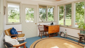 A room with a large window, a wooden desk, a chair, and a woven rug.