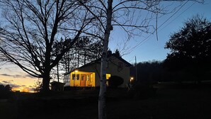 Ein Haus mit sichtbarer Tür und Fenstern, umgeben von Bäumen und blauem Himmel.