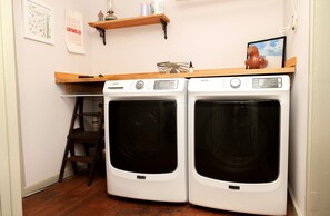 Une buanderie équipée de deux lave-linge Maytag à chargement frontal, d’une étagère en bois sur laquelle sont disposés divers objets, d’une échelle et d’un tableau encadré accroché au mur.