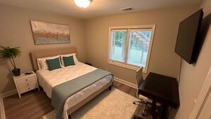 Quarto com cama, mesa de cabeceira, janela e televisão fixada na parede.