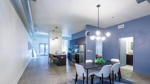 Eine moderne Küche mit dunklen Schränken, einem Edelstahlkühlschrank und einem Essbereich mit dunklem Tisch und weißen Stühlen.