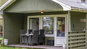 En liten stuga av trä med en veranda, inredd med ett bord och stolar, och en krukväxt.