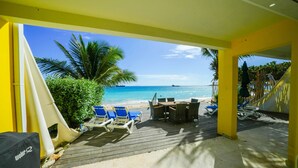 A covered outdoor area with a wooden deck, blue lounge chairs, and a view of the beach and ocean. - Cocos Beachfront Breeze (Simpson Bay)