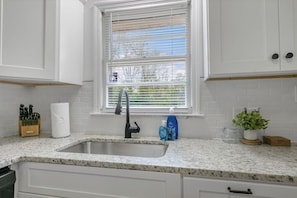 Kitchen features a granite countertop, white cabinetry, and a window with blinds.