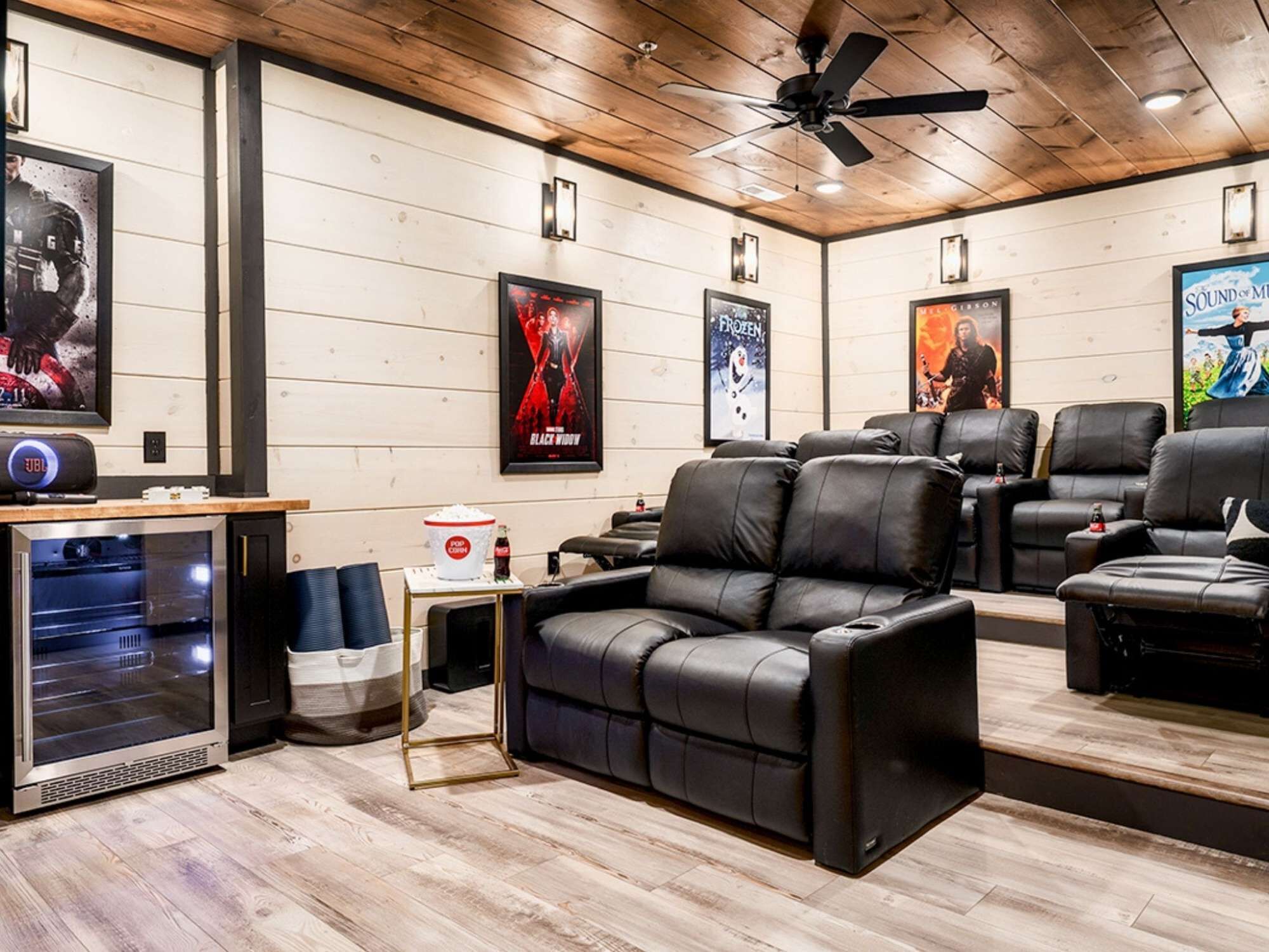 A home theater with reclining leather chairs, a popcorn machine, and movie posters on the wall.