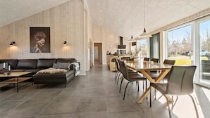 A modern living room with a sofa, dining table, and chairs. There is a kitchen area with a stove and sink visible.