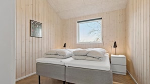 A bedroom with a bed, two bedside tables, a window, and a framed picture on the wall.