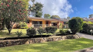 A residential house with a stone retaining wall, a grassy yard, and a clear blue sky.