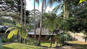 A house with a tiled roof, surrounded by a lush garden with various trees and a well-maintained lawn.
