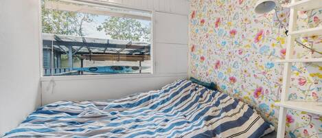 Ett sovrum med en säng, ett fönster med utsikt över en pool och ett hus, och en vägg med blommig tapet.