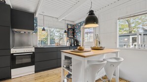 Een moderne keuken met een houten eiland, witte barkrukken, een groot raam en een zwarte hanglamp.