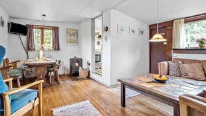 A cozy room with a wooden floor, a dining table, a sofa, a TV, a fireplace, and a window with curtains. - 2 bedroom awesome home in Haarby (Haarby)