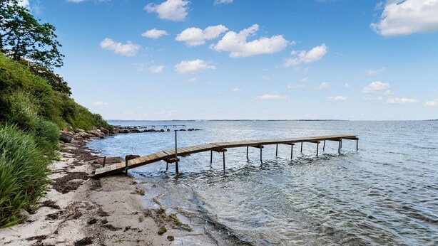 A wooden pier extending into calm waters, surrounded by a sandy beach and greenery. - 2 bedroom awesome home in Haarby (Haarby)